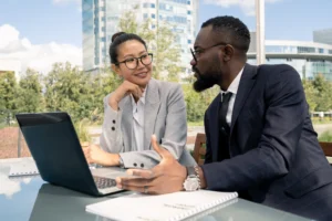 The image shows two business partners discussing new strategies and foreign investment ideas. Both are wearing formal attire.