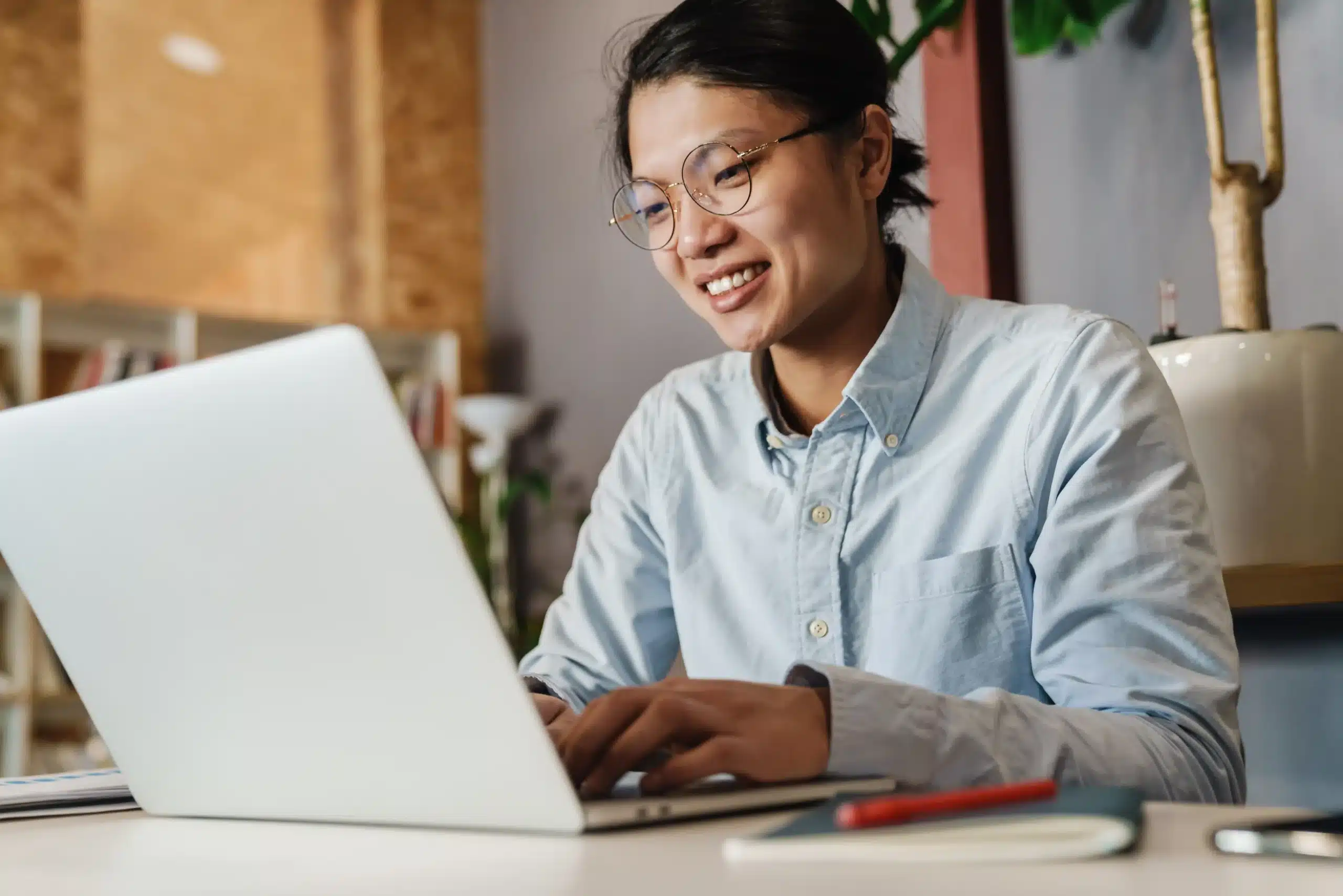 A imagem mostra um homem asiático, satisfeito, sorrindo e estudando com laptop. Ilustra o texto sobre naturalidade.