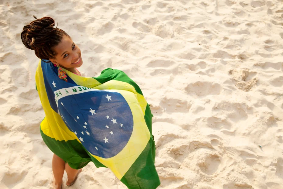 A imagem mostra um retrato aéreo de uma jovem embrulhada na bandeira brasileira, praia de Ipanema, Rio de Janeiro, Brasil. Ilustrando o texto sobre nacionalidade brasileira.