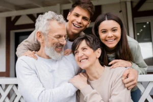 La imagen muestra a unos padres de mediana edad abrazándose con su hija adolescente y su hijo adulto joven en el porche. Y lo ilustra el texto sobre la sucesión familiar.