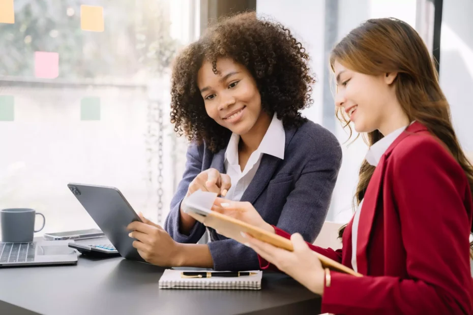 La imagen muestra dos mujeres vestidas formalmente, en un ambiente corporativo, conversando y sonriendo e ilustra el texto: Cómo obtener una visa brasileña invirtiendo en innovación de Koetz Advocacia.