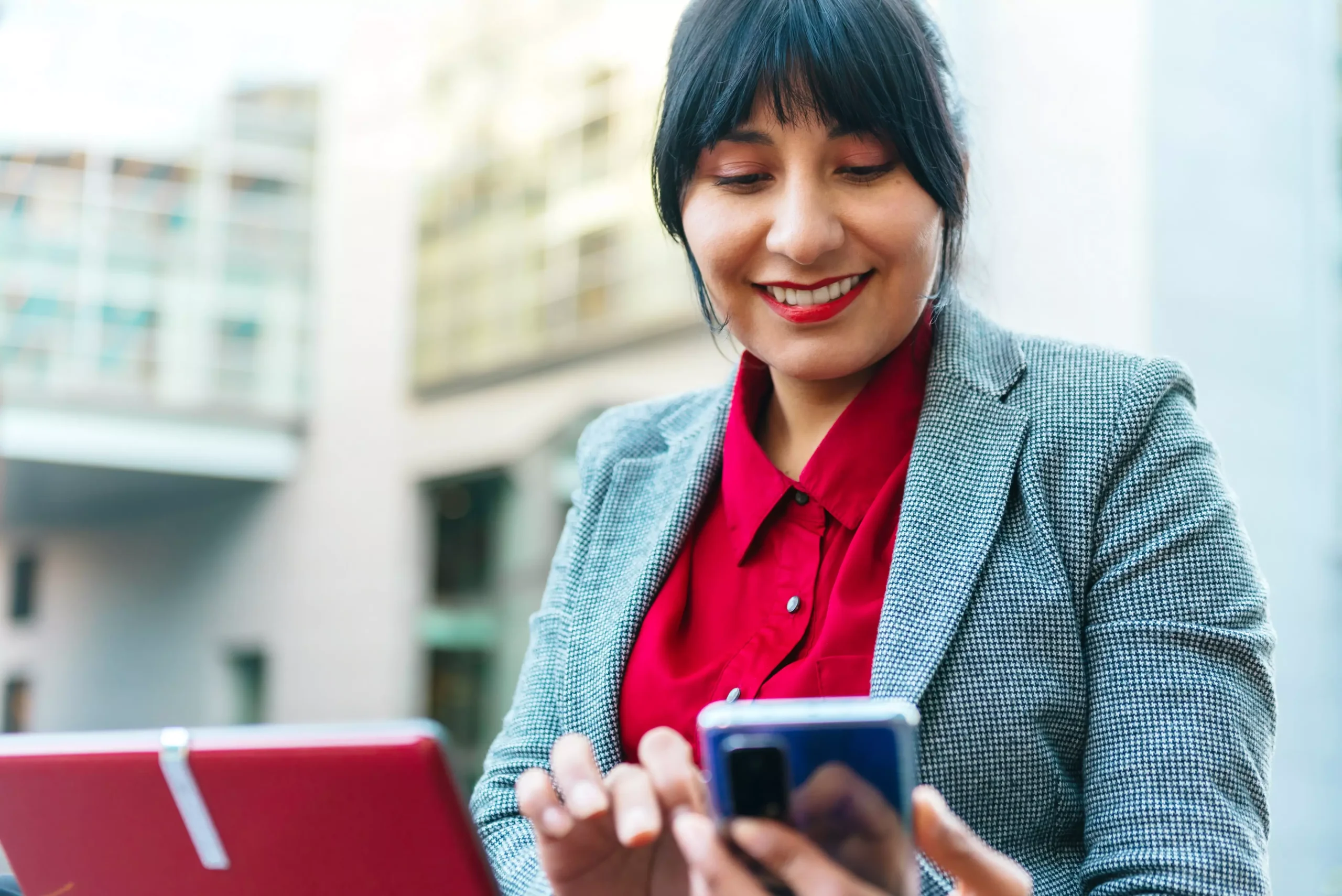 La imagen muestra a una empresaria, vestida formalmente, sosteniendo un teléfono celular, mirando la pantalla y sonriendo e ilustra el texto: Contrato de Representación de Empresa Extranjera en Brasil de Koetz Advocacia.