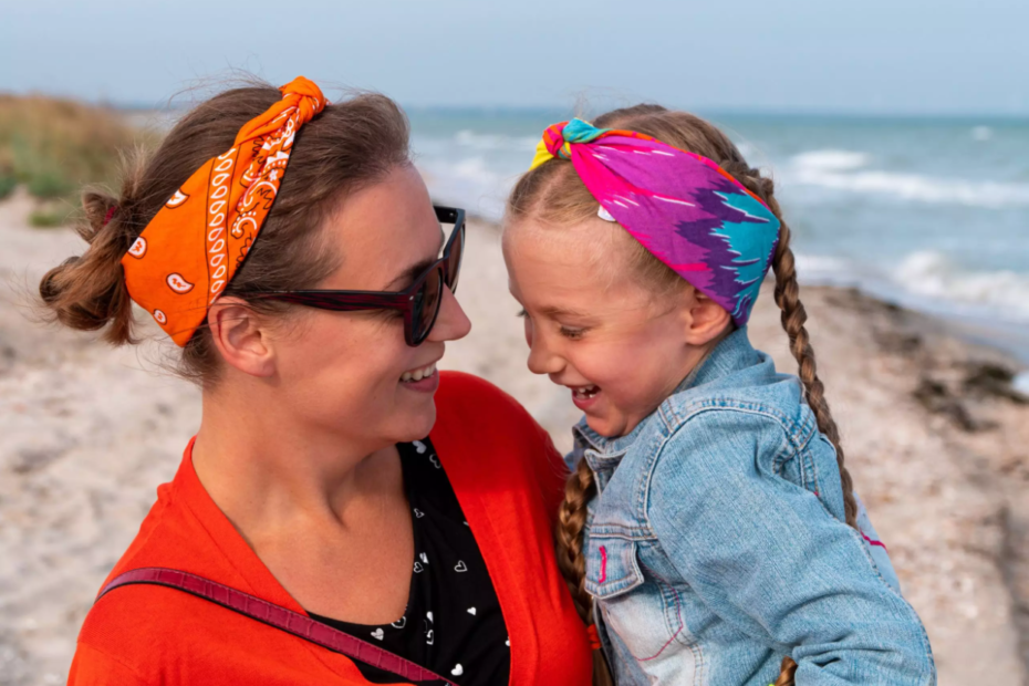 La imagen muestra a una madre y a su hija jugando en la playa, mientras la hija está en el regazo de su madre y ambas sonríen. La imagen ilustra el texto: ¿Puede un inversor extranjero en Brasil obtener una visa para toda la familia? de Koetz Advocacia.