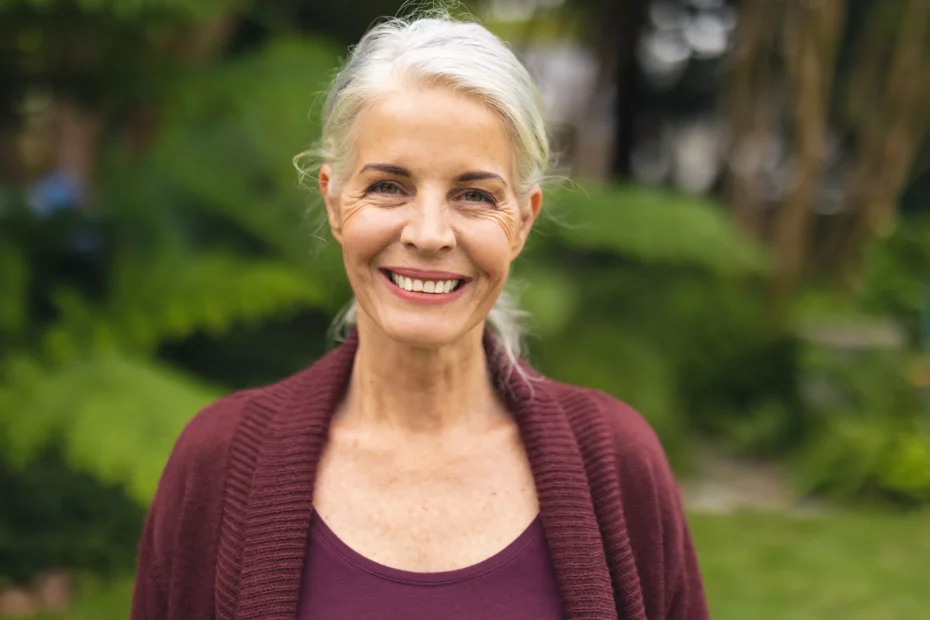 Mujer caucásica mayor sonriendo a la cámara al aire libre e ilustra el texto: Visa de jubilación brasileña: ¿dónde debo pagar el impuesto sobre la renta? de Koetz Advocacia.