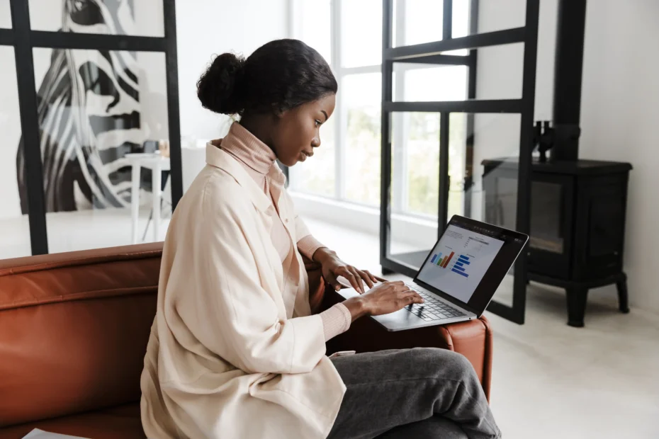 A imagem mostra uma jovem mulher, utilizando o laptop, enquanto está sentada em um sofá, em ambiente externo. Ilustra o texto sobre requisitos para contrato de trabalho.