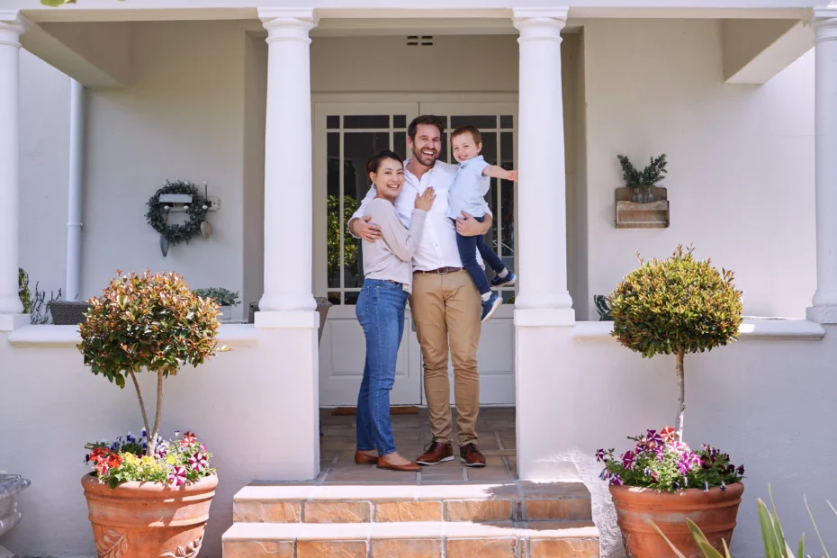 The image shows a couple with their young son on the porch of their house. The three of them smile and look at the camera. It illustrates the text about staying in Brazil by buying property.