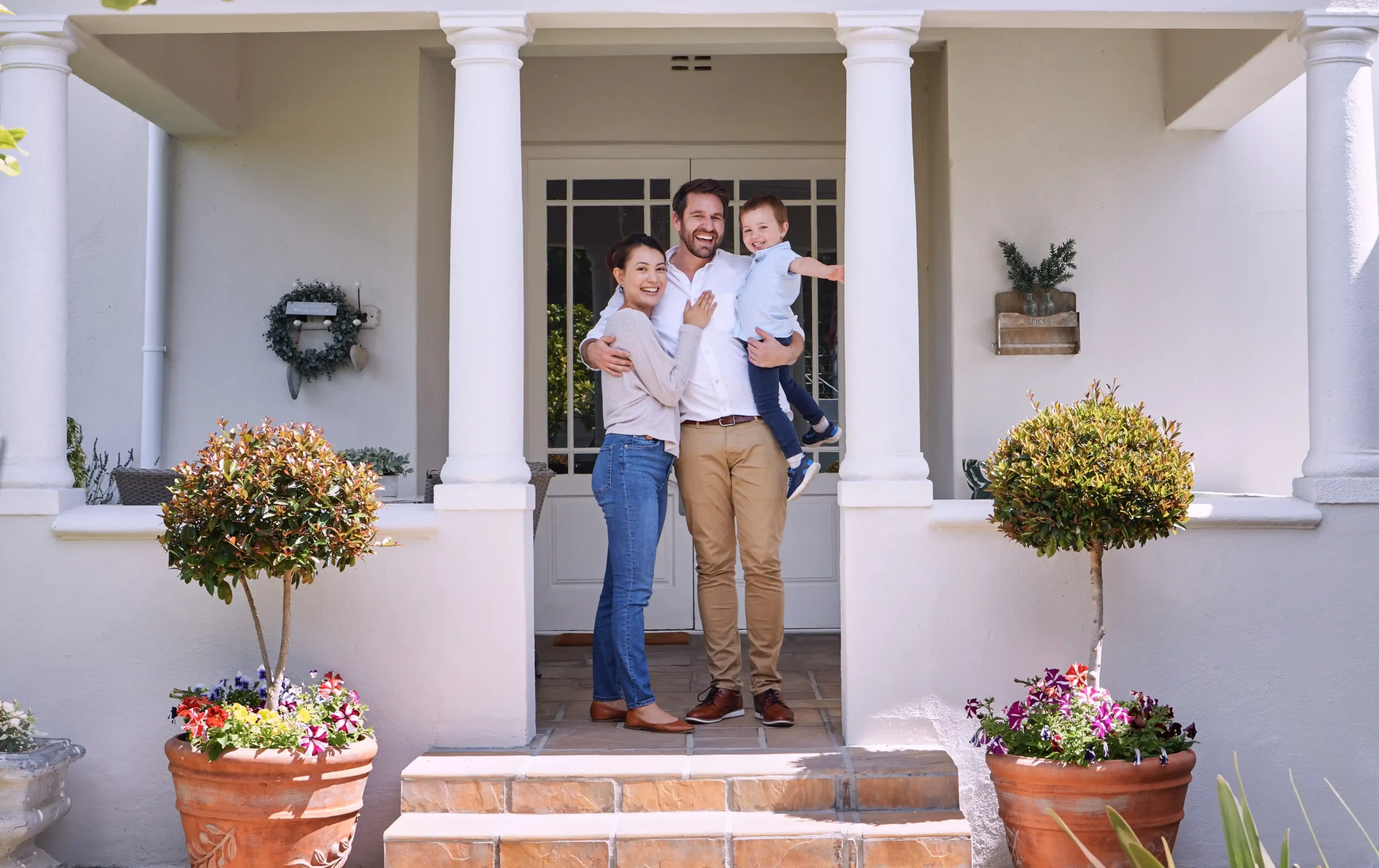 The image shows a couple with their young son on the porch of their house. The three of them smile and look at the camera. It illustrates the text about staying in Brazil by buying property.
