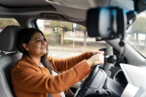 La imagen muestra a una mujer sonriente conduciendo, con las manos en el volante. E ilustra el texto sobre la importación y exportación de vehículos particulares.
