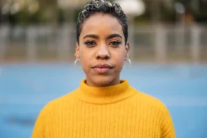 La imagen muestra a una joven de cabello corto y expresión seria, mirando a la cámara. Ilustra el texto sobre extranjeros en situación irregular en Brasil.