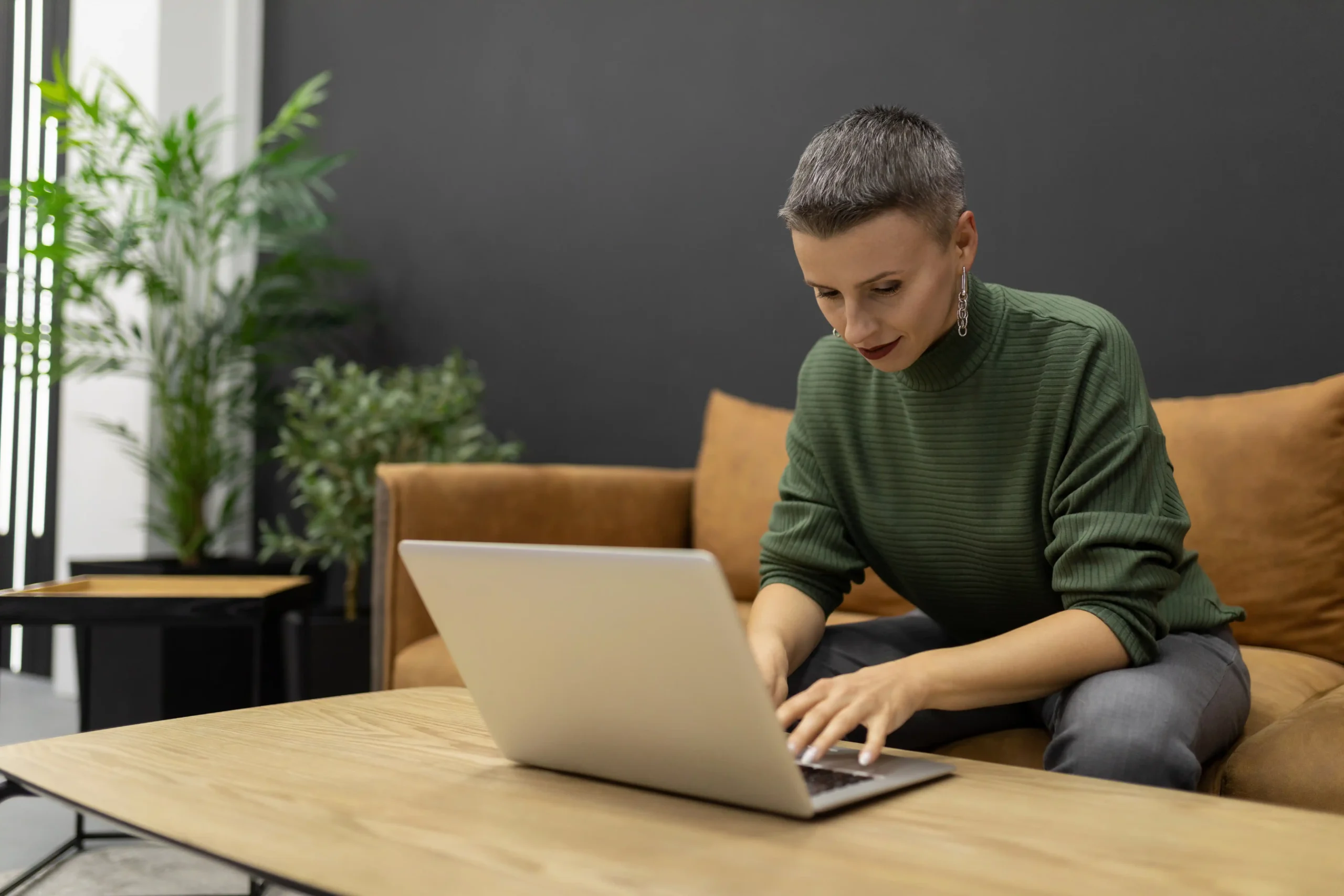 The image shows a woman with a short haircut, working on a laptop while sitting on the couch at home. It illustrates the text about how to obtain an ID card for foreigners.
