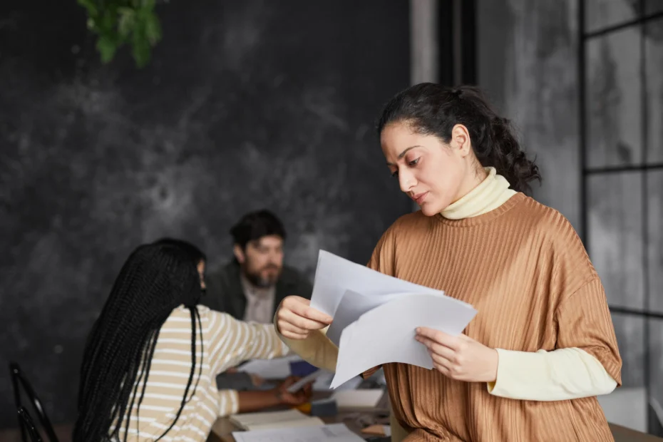 A imagem mostra uma mulher analisando documentos, enquanto participa de uma reunião de traballho. E ilustra o texto sobre contrato de trabalho.
