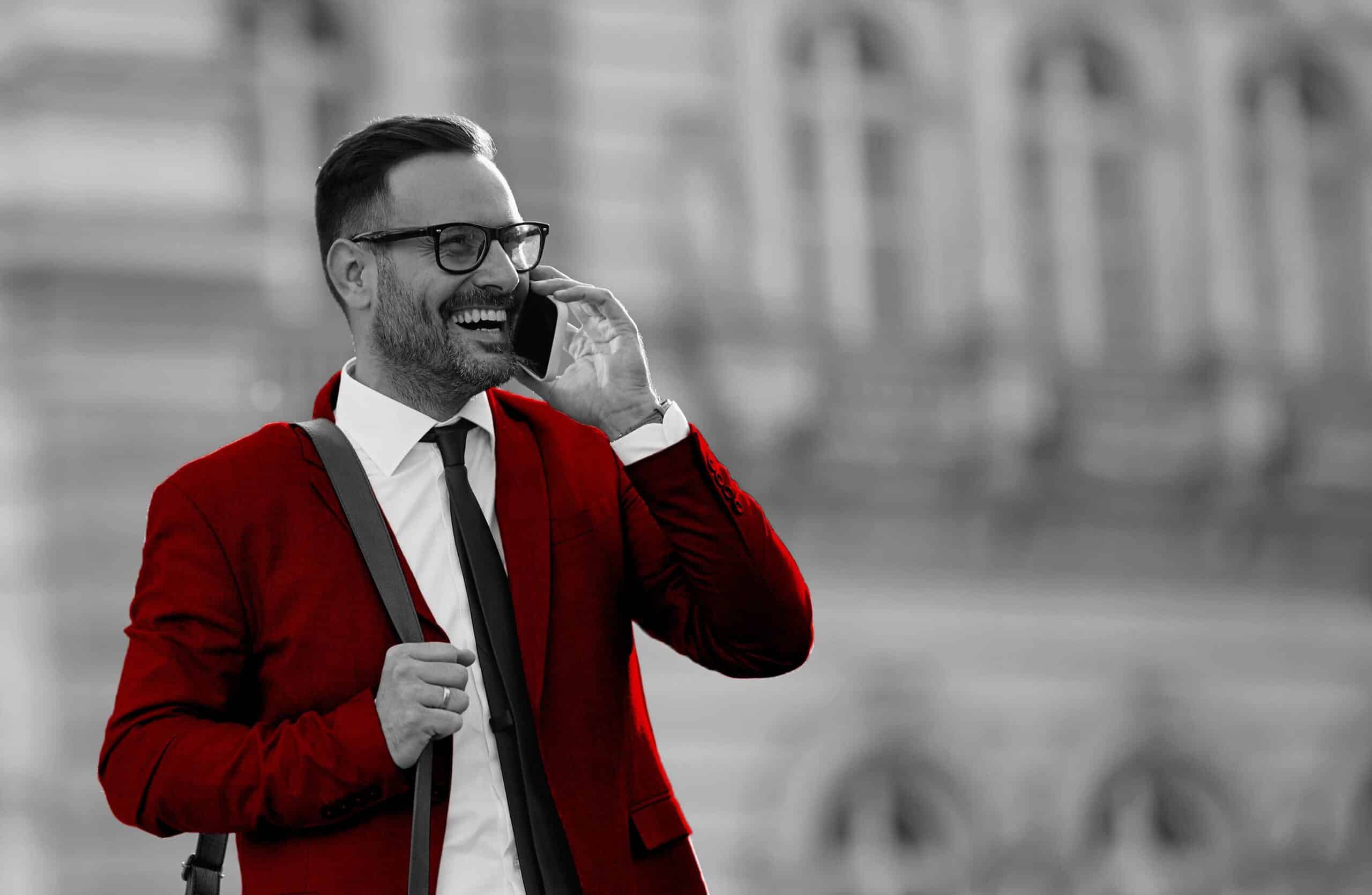 A imagem mostra um homem de terno, falando ao celular e sorrindo.