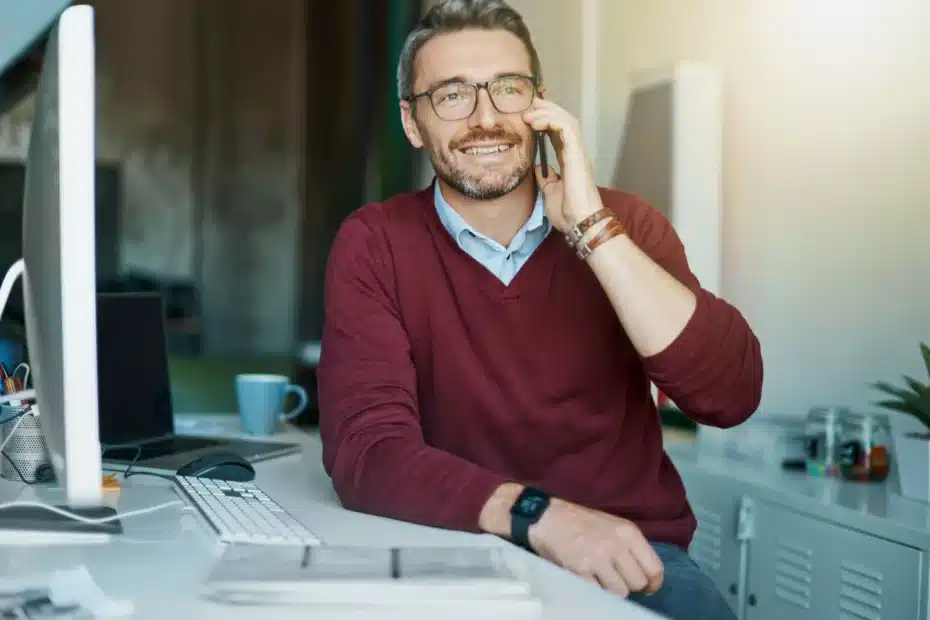 La imagen muestra a un empresario sonriente hablando por un teléfono celular mientras está sentado en una silla de oficina, apoyado en una mesa e ilustra el texto: Préstamo Convertible en Brasil: ventajas del formato en la Colección de Inversión Extranjera de Koetz Advocacia.