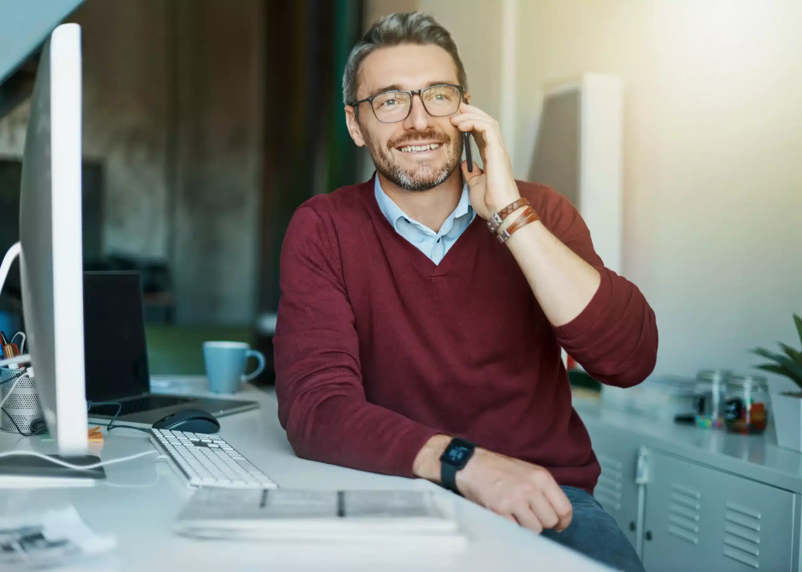 La imagen muestra a un empresario sonriente hablando por un teléfono celular mientras está sentado en una silla de oficina, apoyado en una mesa e ilustra el texto: Préstamo Convertible en Brasil: ventajas del formato en la Colección de Inversión Extranjera de Koetz Advocacia.