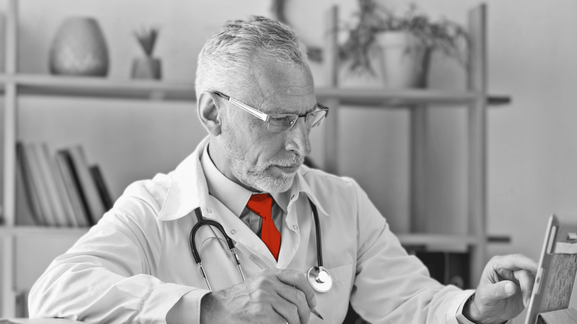 A imagem mostra um médico de meia idade, em seu consultório, de jaleco e estetoscópio em volta do pescoço.