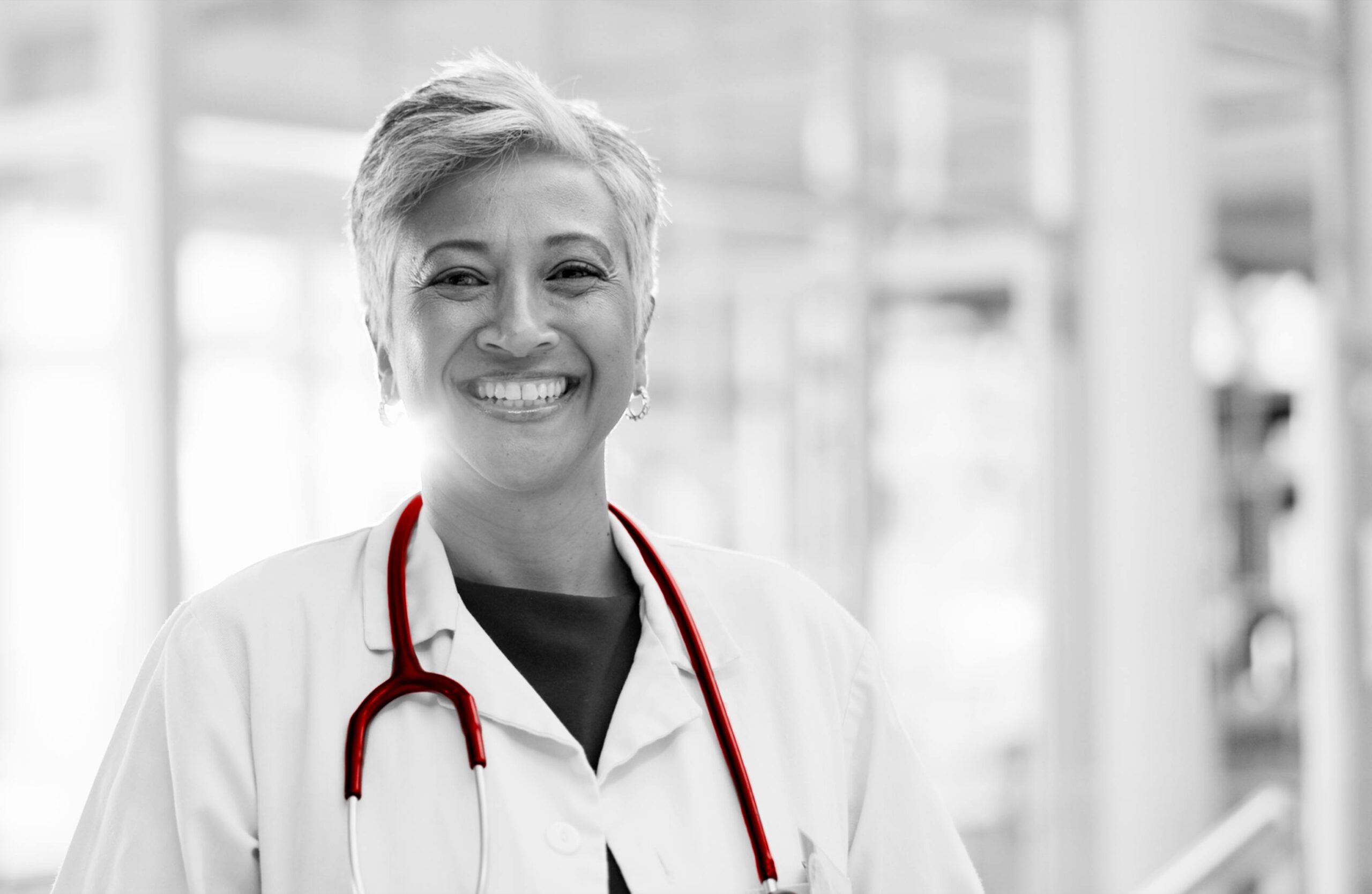 A imagem mostra uma média de meia idade, de cabelos curtos, sorrindo para a câmera. Ela usa jaleco e estetoscópio.