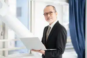La imagen muestra a un empresario de mediana edad consultando su portátil en un entorno corporativo. Ilustra el texto sobre un contrato de subcontratación.