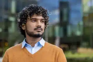 La imagen muestra a un joven con expresión seria, mirando al horizonte. Ilustra el texto sobre los servicios de apoyo a refugiados.