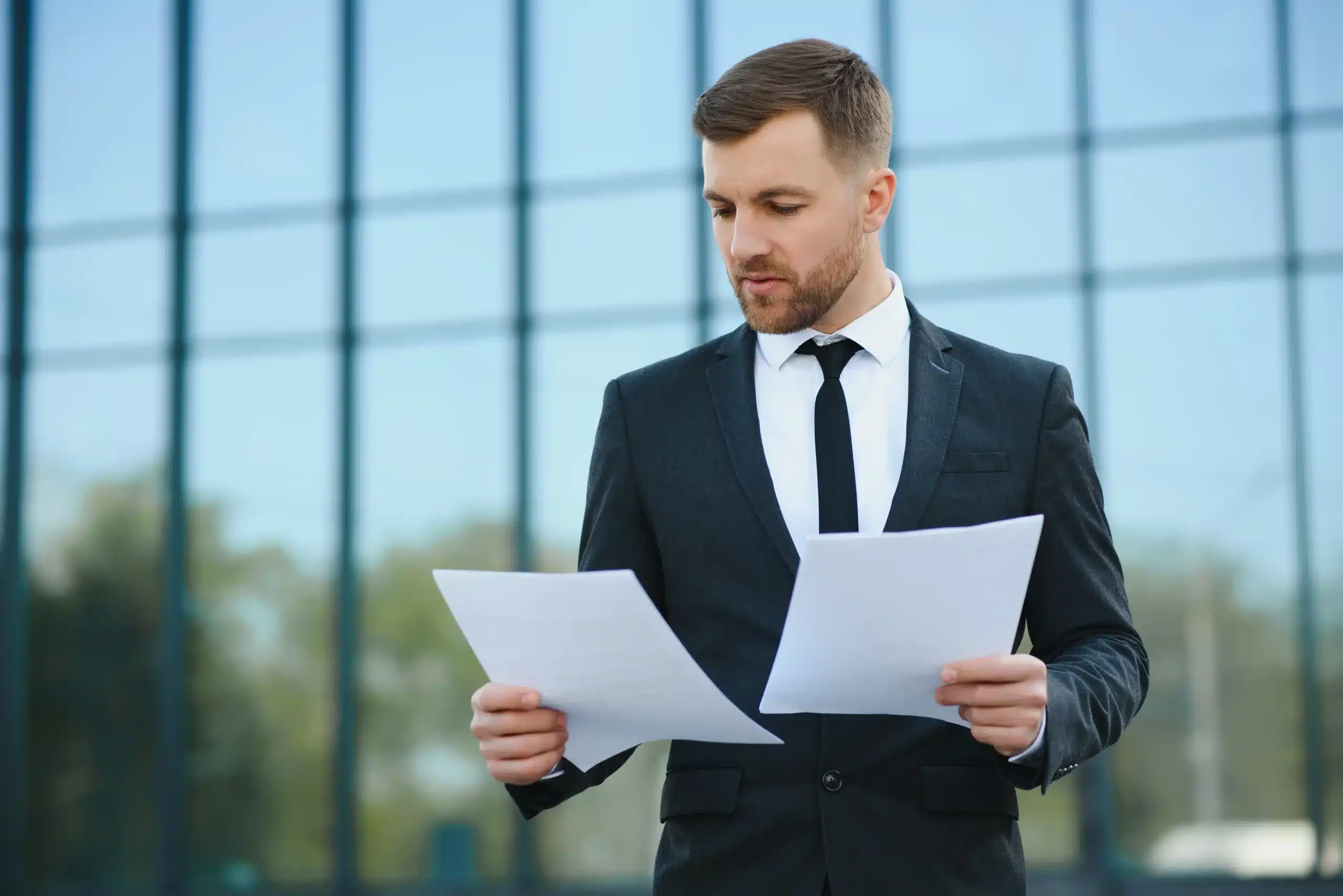 La imagen muestra a un joven empresario de traje analizando documentos. Ilustra el texto de los estatutos sociales o las solicitudes sociales.