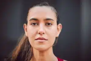 The image shows a serious young woman with her hair tied in a ponytail, looking at the camera. It illustrates the text about refugee immigrant asylum seeker.