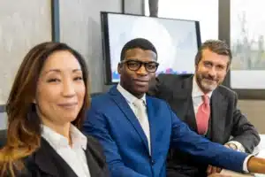 The image depicts three business partners, standing together in a corporate setting, looking at the camera. It illustrates the text on the social contract.