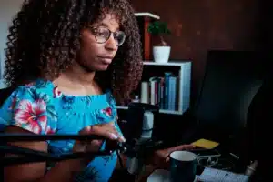 The image shows a young woman using a microphone and computer while broadcasting a podcast from home. It illustrates the text about foreigner to work in Brazil.