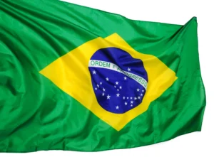 La imagen muestra la bandera brasileña ondeando al viento. Ilustra el texto sobre Embajadas y Consulados en Brasil.