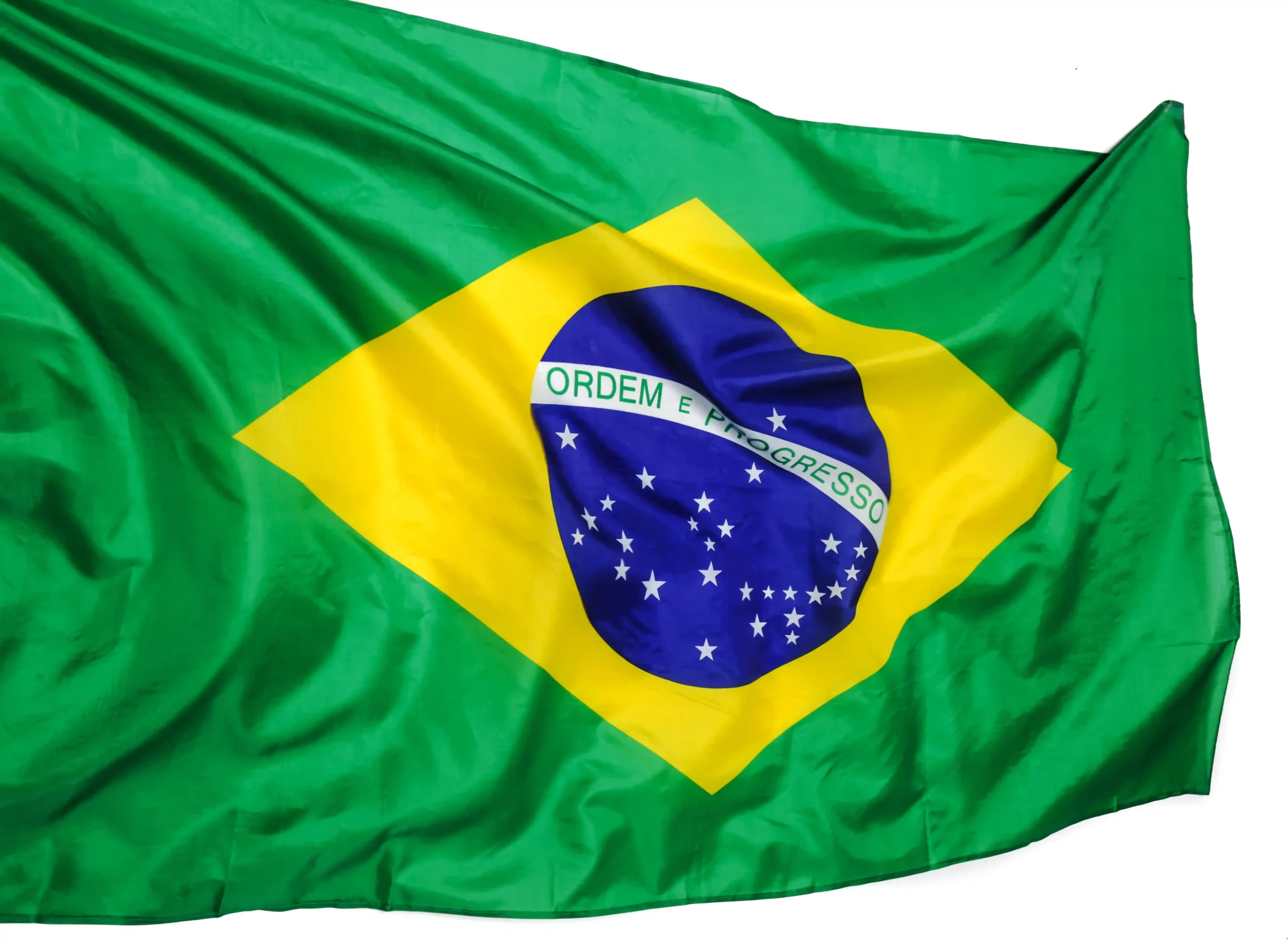 La imagen muestra la bandera brasileña ondeando al viento. Ilustra el texto sobre Embajadas y Consulados en Brasil.