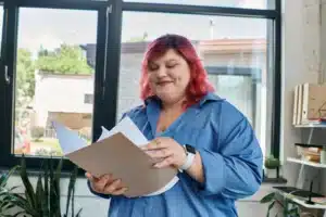 The image shows a young woman with medium-length, pink hair reading a document. It illustrates the text about the Provisional National Migration Registration Document.
