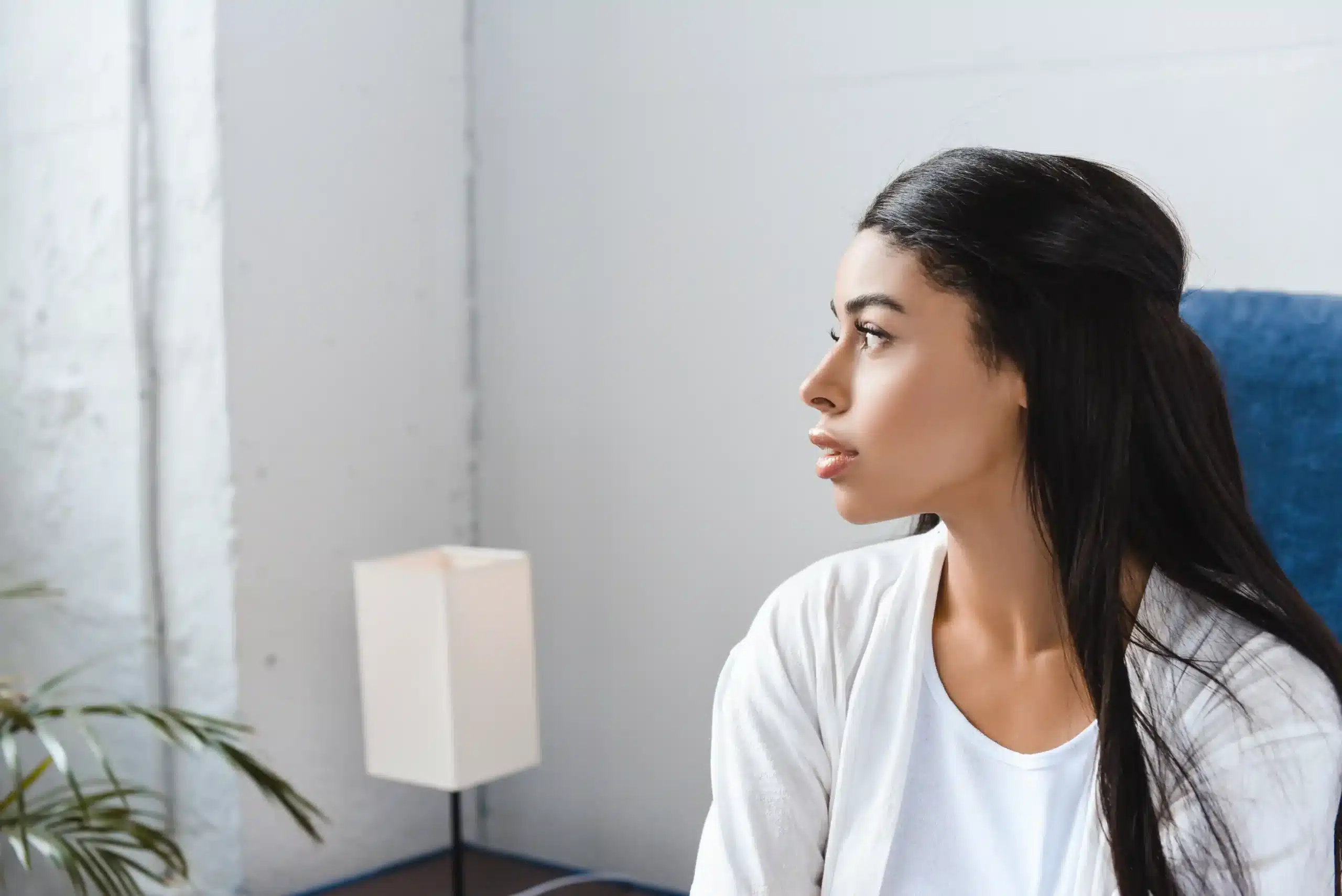 The image shows a young woman, in profile, looking out a window in her home. It illustrates the text about refugees in Brazil.