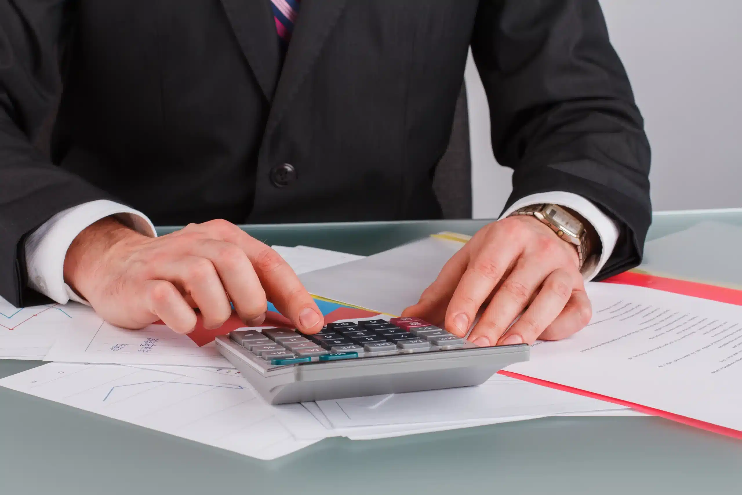 La imagen muestra a un empresario usando una calculadora. Ilustra el texto sobre el acuerdo de doble imposición.