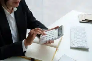 The image shows a businesswoman's hand performing calculations on a calculator held in both hands. It illustrates the text on double taxation agreement.
