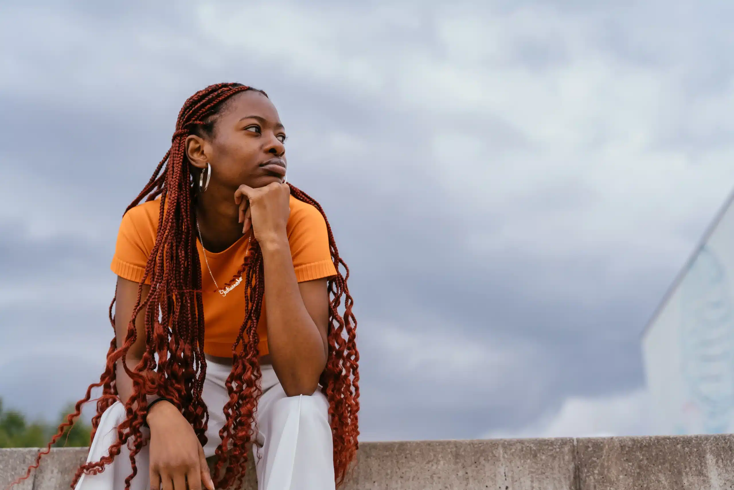 La imagen muestra a una joven negra con trenzas al aire libre, con aspecto pensativo. Ilustra el texto sobre los venezolanos en Brasil.