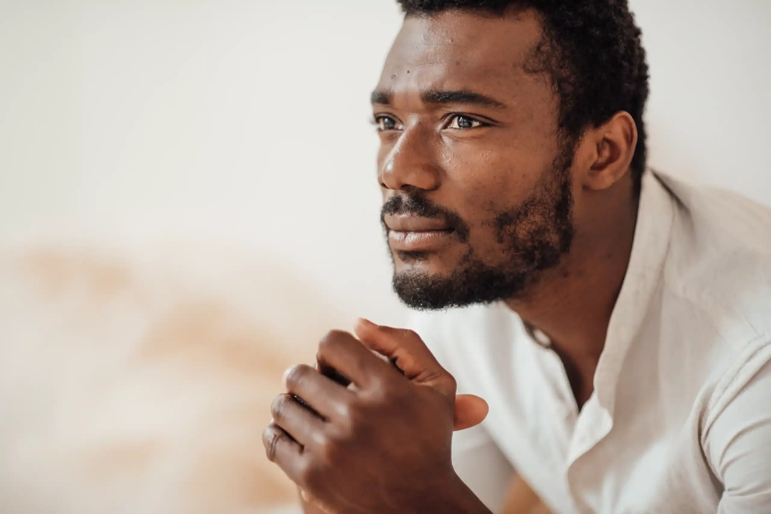 La imagen muestra a un joven negro, pensativo, mirando al horizonte con las manos entrelazadas. Ilustra el texto sobre los refugiados en Brasil.