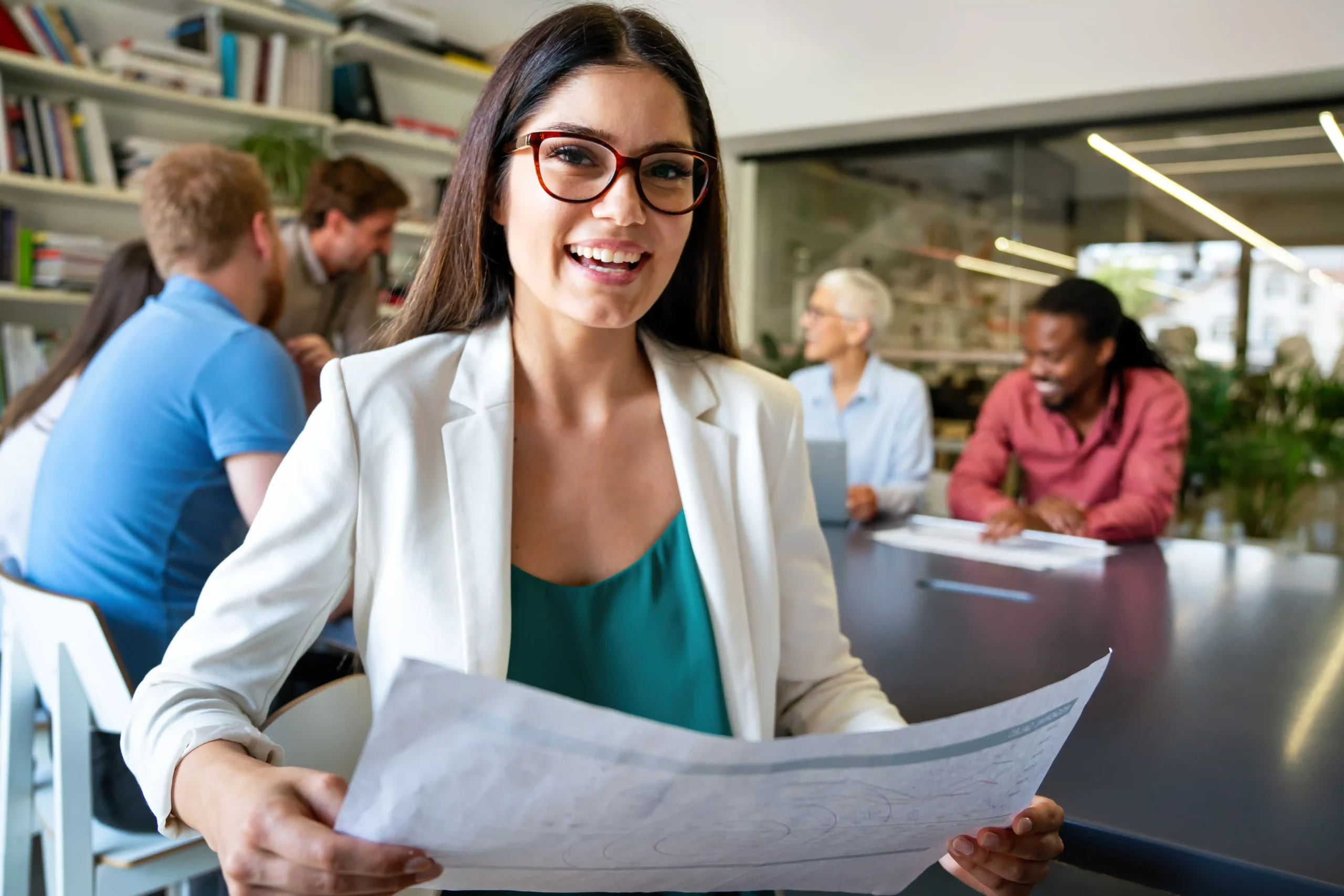 The image shows a young woman smiling, looking at the camera. She is in a meeting in a corporate setting. It illustrates the text about Jobs for foreigners in Brazil.