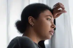 The image shows a young Black woman looking out a window with a thoughtful expression. It illustrates the text about Venezuelans in Brazil.