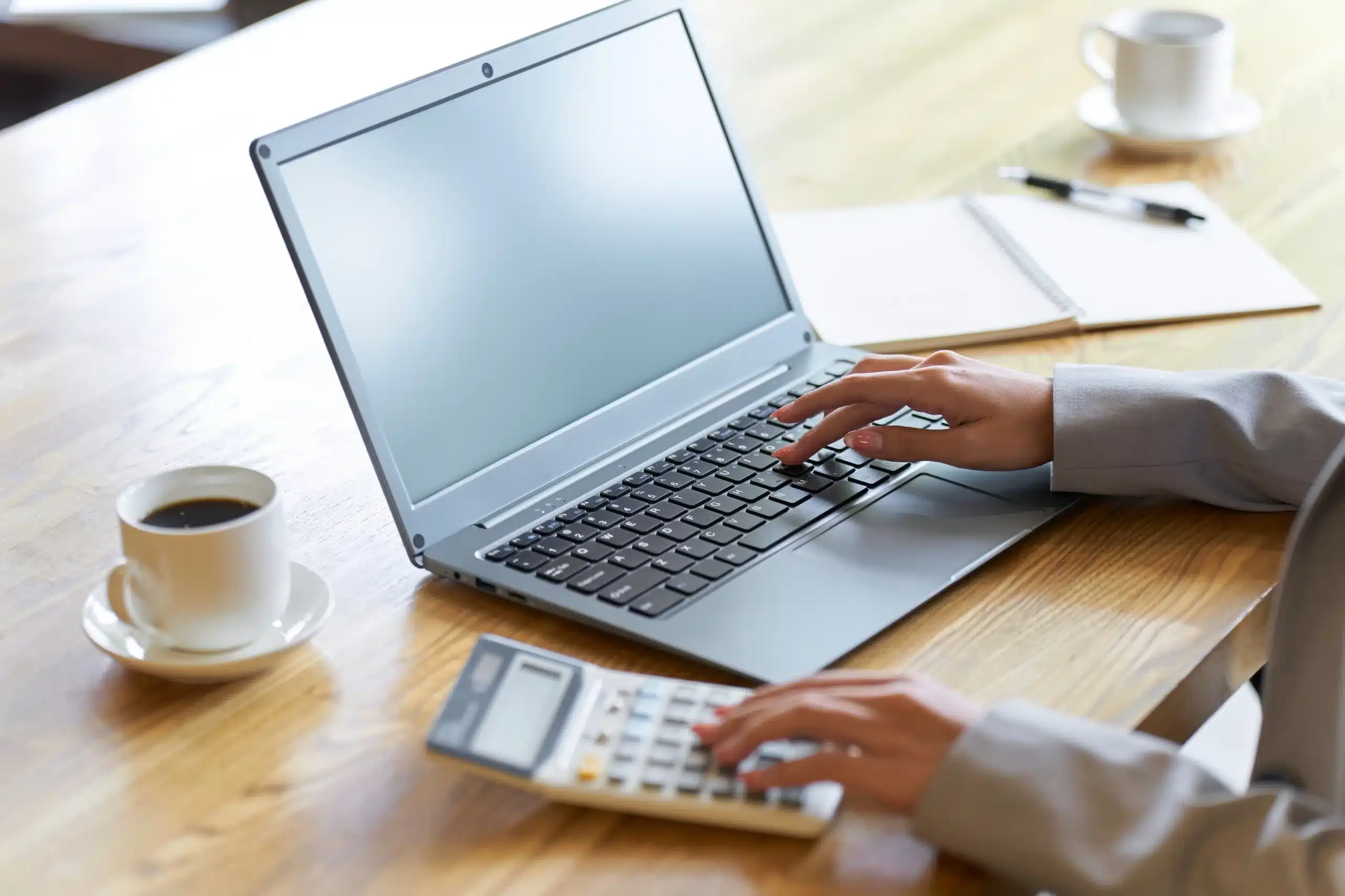 A imagem mostra a m]ao em destaque de uma mulher de negócios, usando o laptop e a calculadora. Ilustra o texto sobre bitributação.