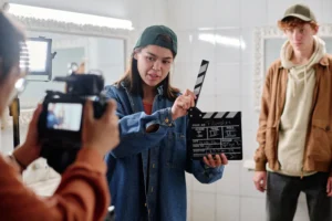 The image shows a filmmaker holding a clapperboard, standing in front of a camera, filming. It illustrates the text on Foreign Filming in Brazil.