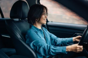 La imagen muestra a una mujer joven, con gafas, sonriendo, conduciendo un automóvil e ilustra el texto sobre Licencia de Conducir Nacional.