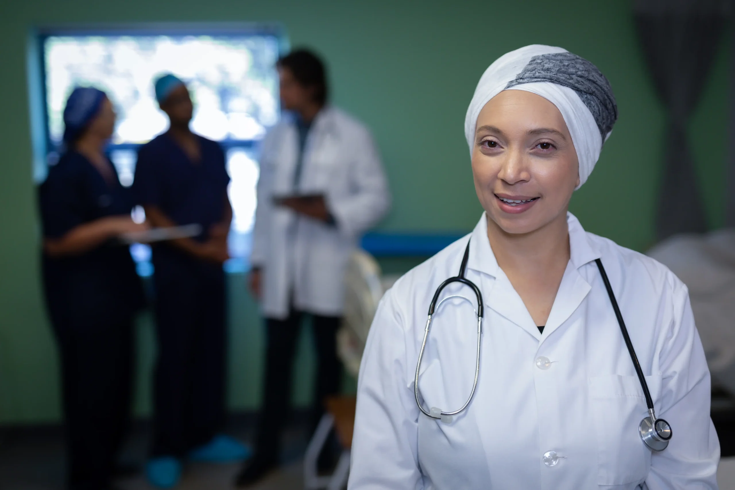 La imagen muestra a una doctora de mediana edad con bata de laboratorio en un hospital. Sonríe a la cámara e ilustra el texto sobre la visa de desarrollo médico.