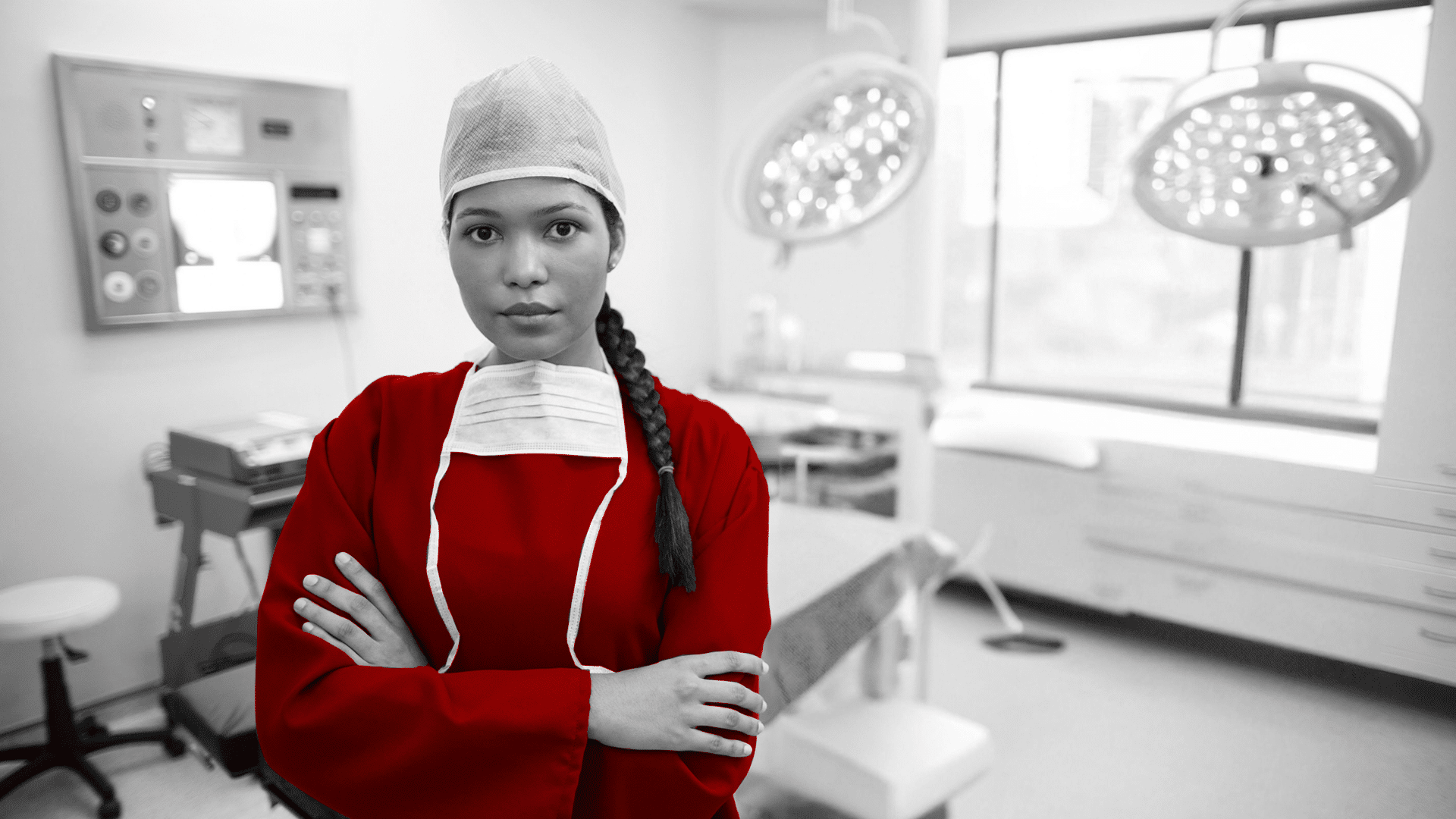 A imagem mostra uma jovem médica, de braços cruzados, expressão séria em ambiente cirúrgico, usando roupas próprias.