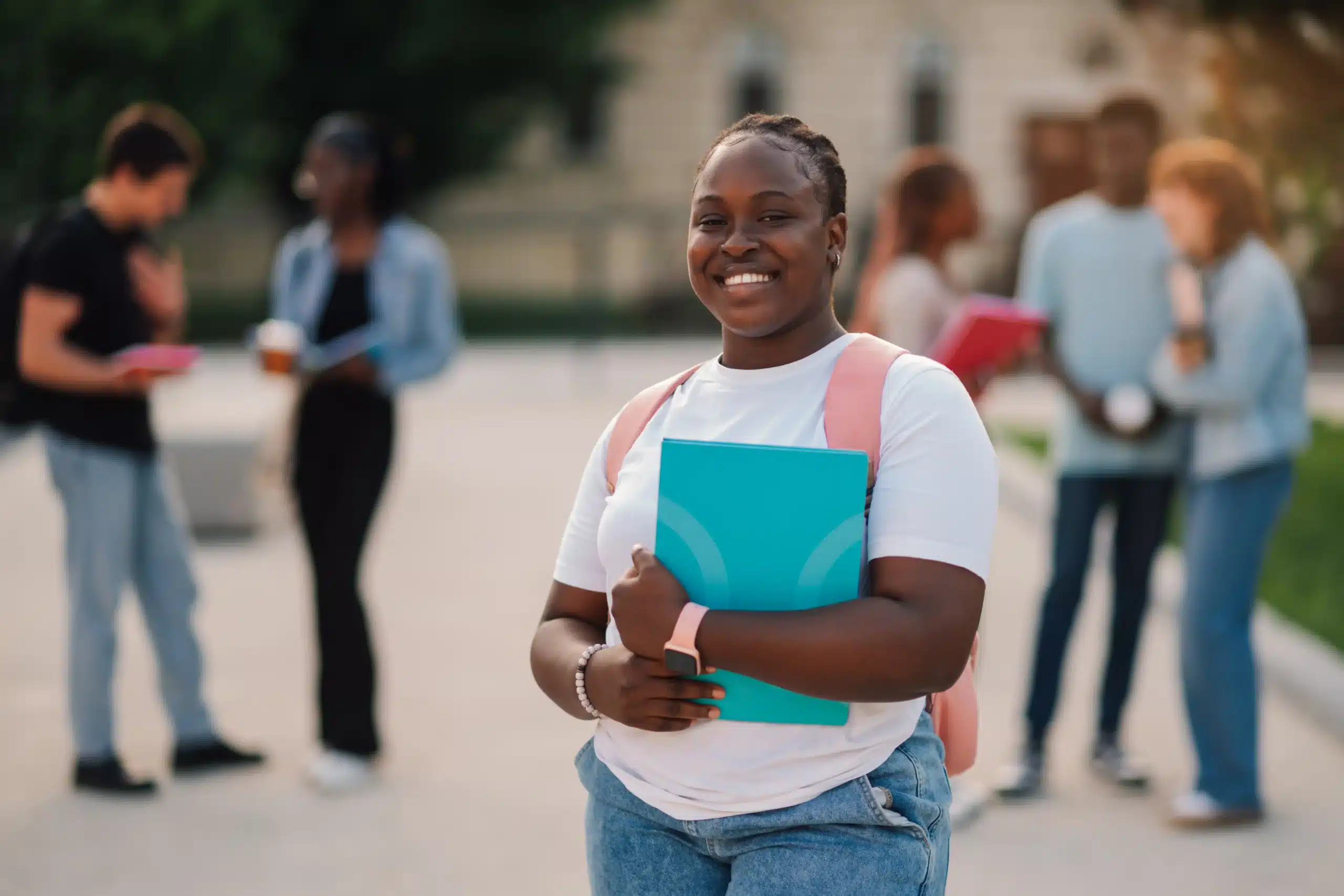 The image shows a young student smiling at the camera while holding a notebook. She is outdoors on her campus. It illustrates the text about visas for academic internships in Brazil.