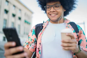 La imagen muestra a un joven al aire libre usando un teléfono inteligente mientras sostiene una taza de café en la otra mano. Ilustra el texto sobre la Igualdad de Derechos en Portugal.