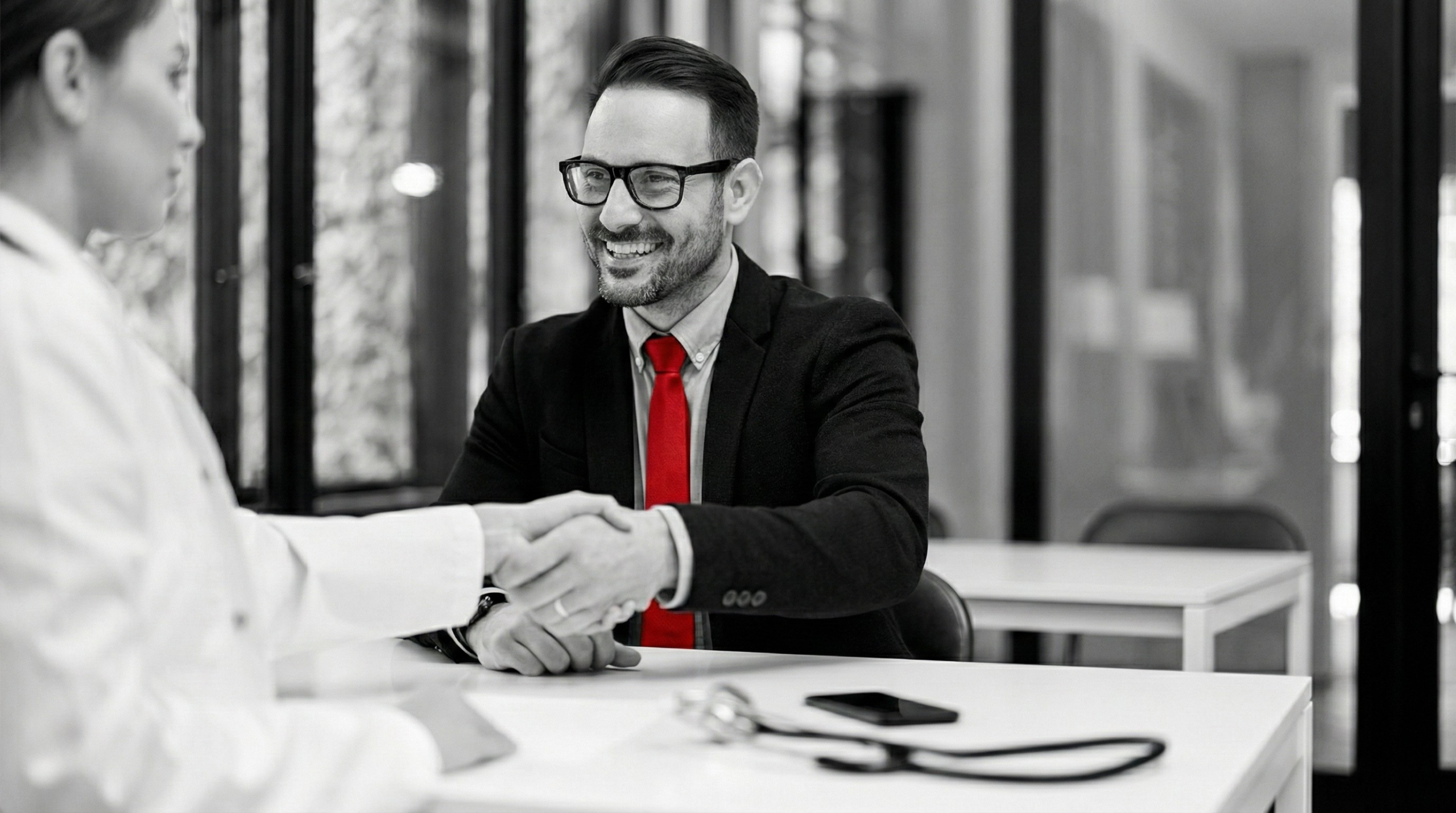 A imagem mostra um advogado apertando a mão de uma médica, enquanto ambos estão sentados à mesa, de frente um para outro.