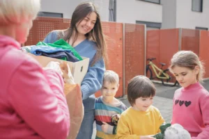 The image shows a woman giving clothes and toys to children, in a volunteer job. Illustrates a text about Volunteer visa in Brazil.