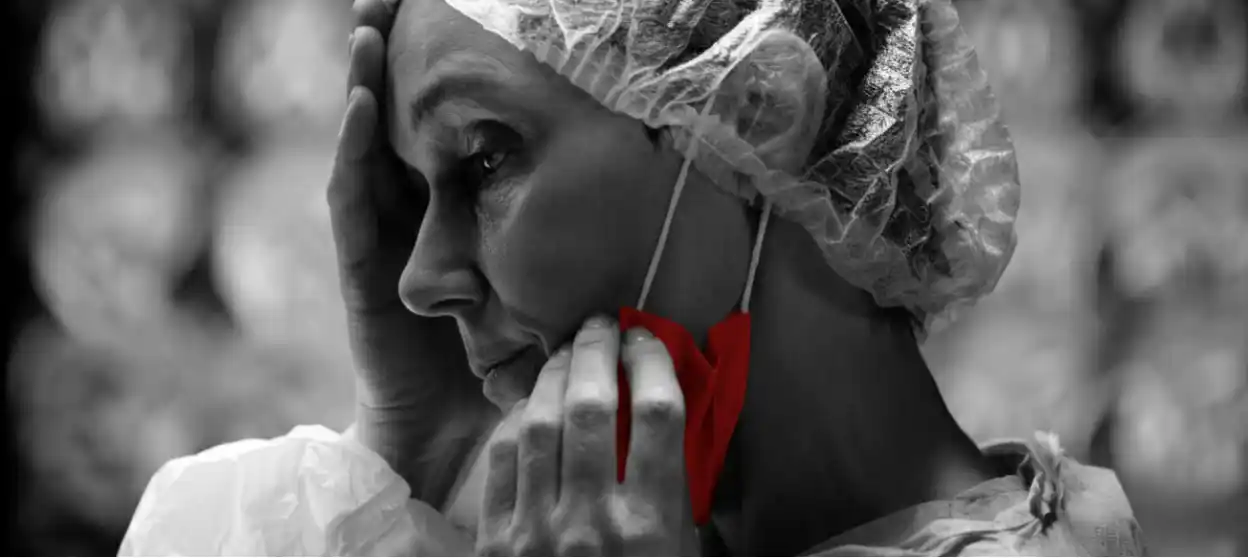 A imagem mostra uma cirurgiã, preocupada, abaixando a máscara com uma das mãos, enquanto segura a testa com a outra.