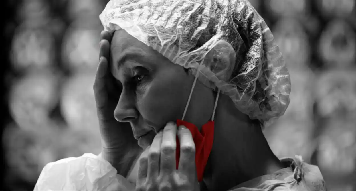 A imagem mostra uma cirurgiã, preocupada, abaixando a máscara com uma das mãos, enquanto segura a testa com a outra.