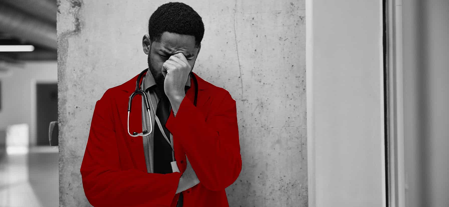 A imagem mostra um jovem médico, de jaleco, estetoscópio em volta do pescoço, com uma expressão preocupada, segurando o rosto com uma das mãos.