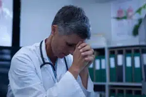 A imagem mostra uma médica de meia-idade, com as mãos encostadas na testa, preocupada. Ilustra o texto sobre Perda da chance na responsabilidade civil médica.