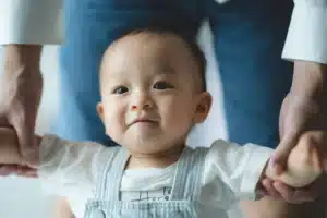 La imagen muestra a un bebé al que su padre ayuda a caminar. Ilustra el texto sobre la Visa brasileña para adopción.